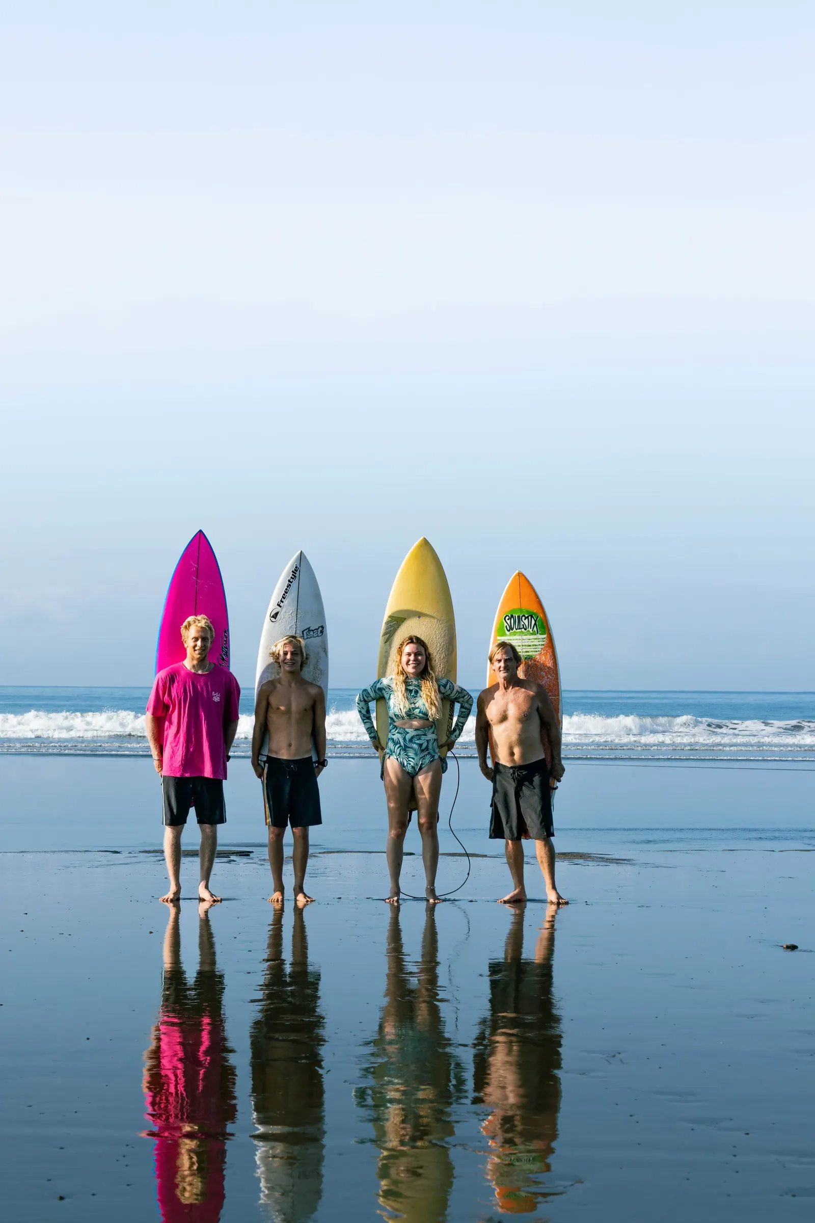 Surfers and boards reflected on the wet sand